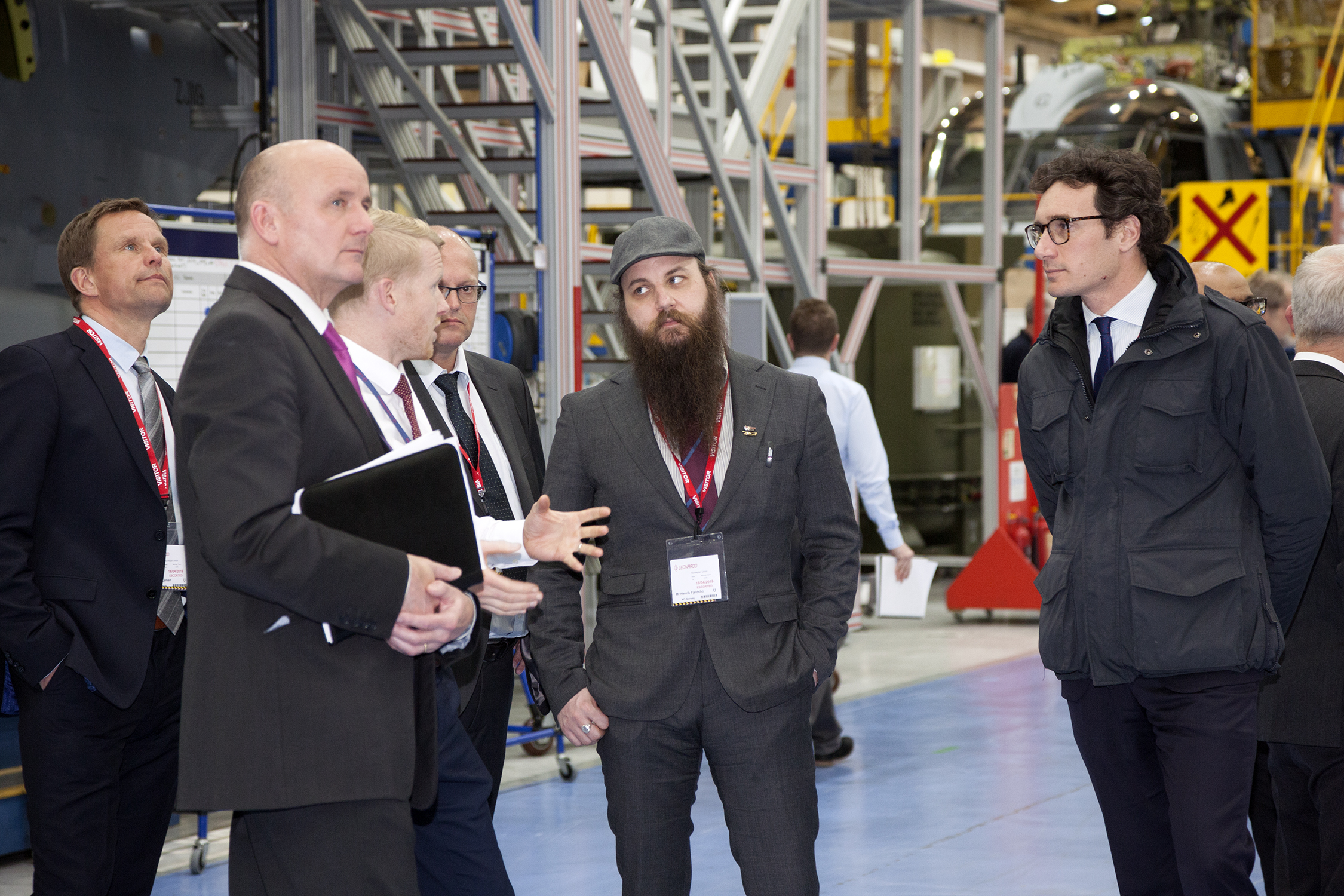 Henrik Fjeldsbø (midt i bildet) lytter til informasjonen fra Leonardos representanter ved fabrikken. I bakgrunnen ses en militær Aw101 som er under bygging. Foto: Leonardo